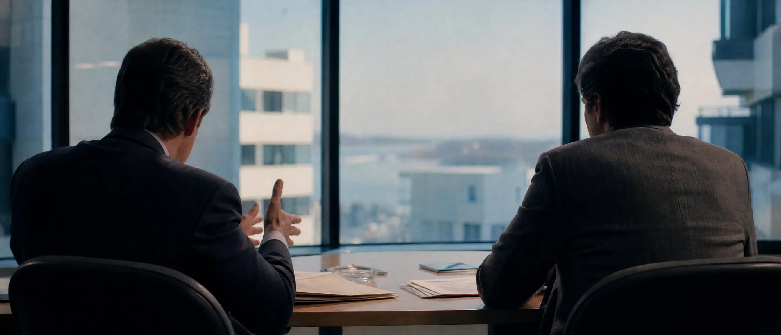 Dos personas de espaldas conversan en una mesa de reuniones frente a un gran ventanal